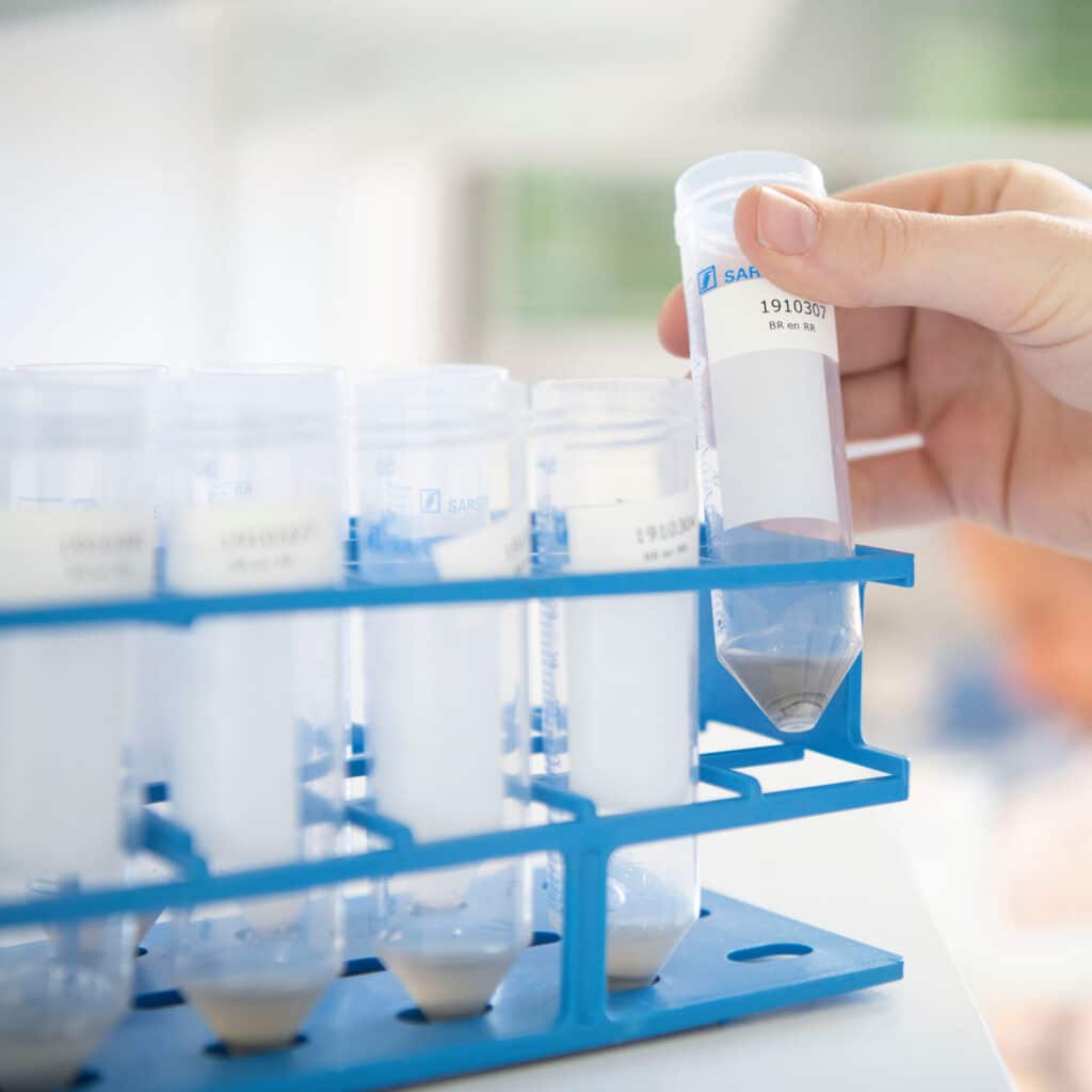 Laboratoriummedewerker plaatst reageerbuis met monster in rek tijdens kwaliteitscontrole