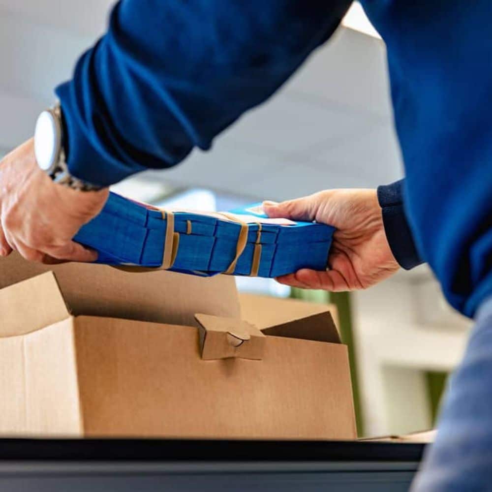 Medewerker pakt stapels blauwe certificaten in voor verzending